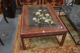 A Chinese red lacquer coffee table with glass top enclosing an on laid and inlaid panel depicting