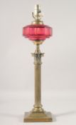 A BRASS CORINTHIAN COLUMN OIL LAMP with cranberry glass reservoir, (converted to electricity). 22ins