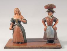 A PAINTED WOOD FOLK ART STAND with two figures. 11.5ins high.