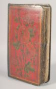 AN OTTOMAN LEATHER BOUND QURAN with lacquered floral covers, 25.5cm x 15.5cm.