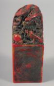 A CHINESE RED STAINED SOAPSTONE SEAL carved with a dragon. 6ins high.