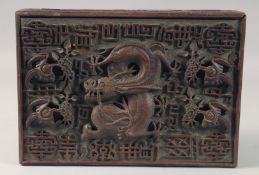 A CHINESE CARVED HARDWOOD BOX with a hinged cover depicting a dragon. 12ins wide.