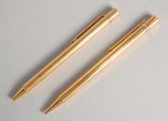 TWO CARTIER GILT PENS in a red pouch.