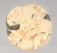 A JAPANESE BONE NETSUKE carved with faces. 4cm diameter.