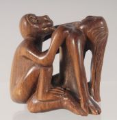AN EROTIC CARVED WOOD NETSUKE modelled as a woman engaged in intercourse with a monkey.