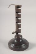 AN EARLY METAL CANDLESTICK on a circular wooden base. 8ins high.