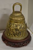 A decorative brass bell on a Chinese wooden stand.