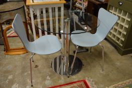 A circular glass and chrome dining table with a pair of chairs.
