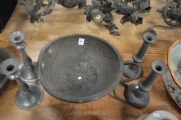 A pewter colander and two pairs of pewter candlesticks.