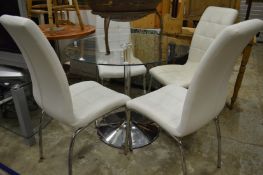 A circular glass and chrome dining table with four chairs.