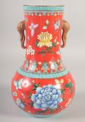 A CHINESE RED GROUND TWIN HANDLE VASE, painted with flora and butterflies, the handles molded as