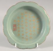 A CHINESE CELADON CALLIGRAPHIC DISH, with incised inscription and gilded petal form rim, 19cm wide.