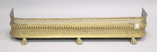 A REGENCY PIERCED BRASS FENDER with pierced decoration supported on three cast brass claw feet.