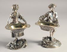 A PAIR OF SILVER PLATED YOUNG BOY AND GIRL SALTS both carrying baskets. 5.5ins high.