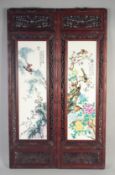 A PAIR OF UPRIGHT CHINESE PORCELAIN PANELS, birds and flowers in wooden frames.