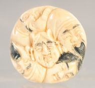 A CARVED BONE CIRCULAR FACES NETSUKE. 1.5ins diameter.