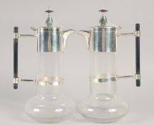 A GOOD PAIR OF CHRISTOPHER DRESSER STYLE GLASS AND SILVER PLATE CLARET JUGS with ebony handles.