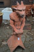 A terracotta coloured garden ornament modelled as a gargoyle on a ridge tile.