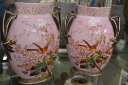 A pair of large decorative twin handled vases, pink ground painted with birds and flowers.