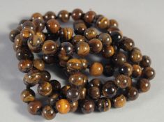 A STRING OF OVER ONE HUNDRED TIGERS EYE BEADS. 33ins long.
