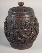 A CHINESE CARVED HARDWOOD JAR AND COVER, with relief carving depicting dragons, 15.5cm high.