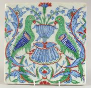 AN IZNIK GLAZED POTTERY TILE, painted with birds and floral sprays, 25.5cm square.