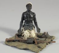 A GOLD PAINTED BRONZE GROUP of an Arab man kneeling, guns before him. 4ins high.