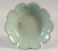 A CHINESE CELADON CALLIGRAPHIC PETAL FORM DISH, with incised inscription and gilded rim, 18cm wide.
