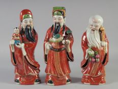 THREE CHINESE CORAL RED PORCELAIN FIGURES of immortals, each with impressed mark to base, 28cm, 29cm