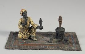 A COLD PAINTED BRONZE GROUP, the amulet vendor sitting on a rug. 7ins long.