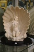 An Art Deco style table lamp modelled as a seated female nude within a shell on a wooden base.