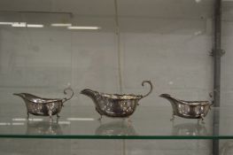 A pair of small silver sauce boats and a similar larger sauce boat.