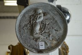 A circular cast lead plaque depicting an angel.