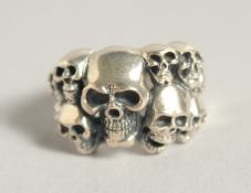 A SILVER RING WITH TEN SKULLS.