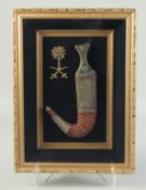 A FRAMED AND GLAZED JAMBIYA IN SCABBARD, with mounted emblem.