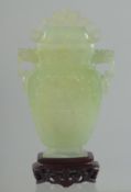 A CHINESE CARVED JADE LIDDED VASE AND WOODEN STAND, the vase with archaic style carving and drop