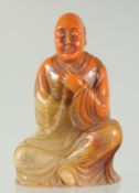 A CHINESE AMBER-COLOUR SOAPSTONE LUOHAN FIGURE, seal characters to base, 11.5cm high.