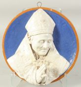 A CONTINENTAL GLAZED POLYCHROME TERRA COTTA ROUNDEL of a praying Bishop on a blue background. 32cm