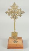 A BRASS CROSS on a wooden stand, with gemstones. 11.5ins high
