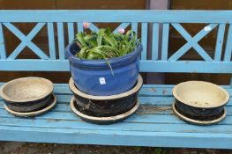 A blue glazed plant pot with plants and a set of three black glazed planters with bases.