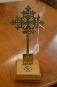 A brass cross on a wooden base, the base set with various gem stones.