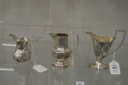 A silver helmet shaped pedestal cream jug and two other jugs.
