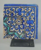 A PERSIAN QAJAR GLAZED POTTERY CORNER TILE, on a fitted metal stand, the tile painted with foliate