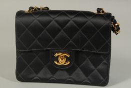A CHANEL PADDED BLACK EVENING BAG with gilt interior, 6.5ins long, with a gilt metal and black