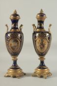 A PAIR OF SEVRES DESIGN DEEP BLUE PORCELAIN AND GILT METAL VASES AND STANDS. 18ins high.