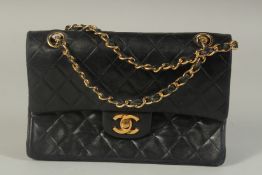 A CHANEL BLACK PADDED LEATHER BAG, 8ins long with entwined gilt and leather chain, 14ins long.