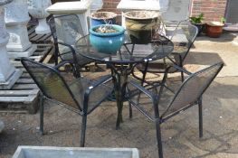 A circular black painted metal patio table with four armchairs and a parasol base.