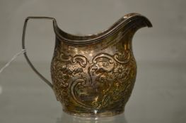 A silver milk jug with embossed decoration.