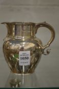 A silver cream jug with scroll handle.