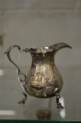 A small silver cream jug with embossed decoration.